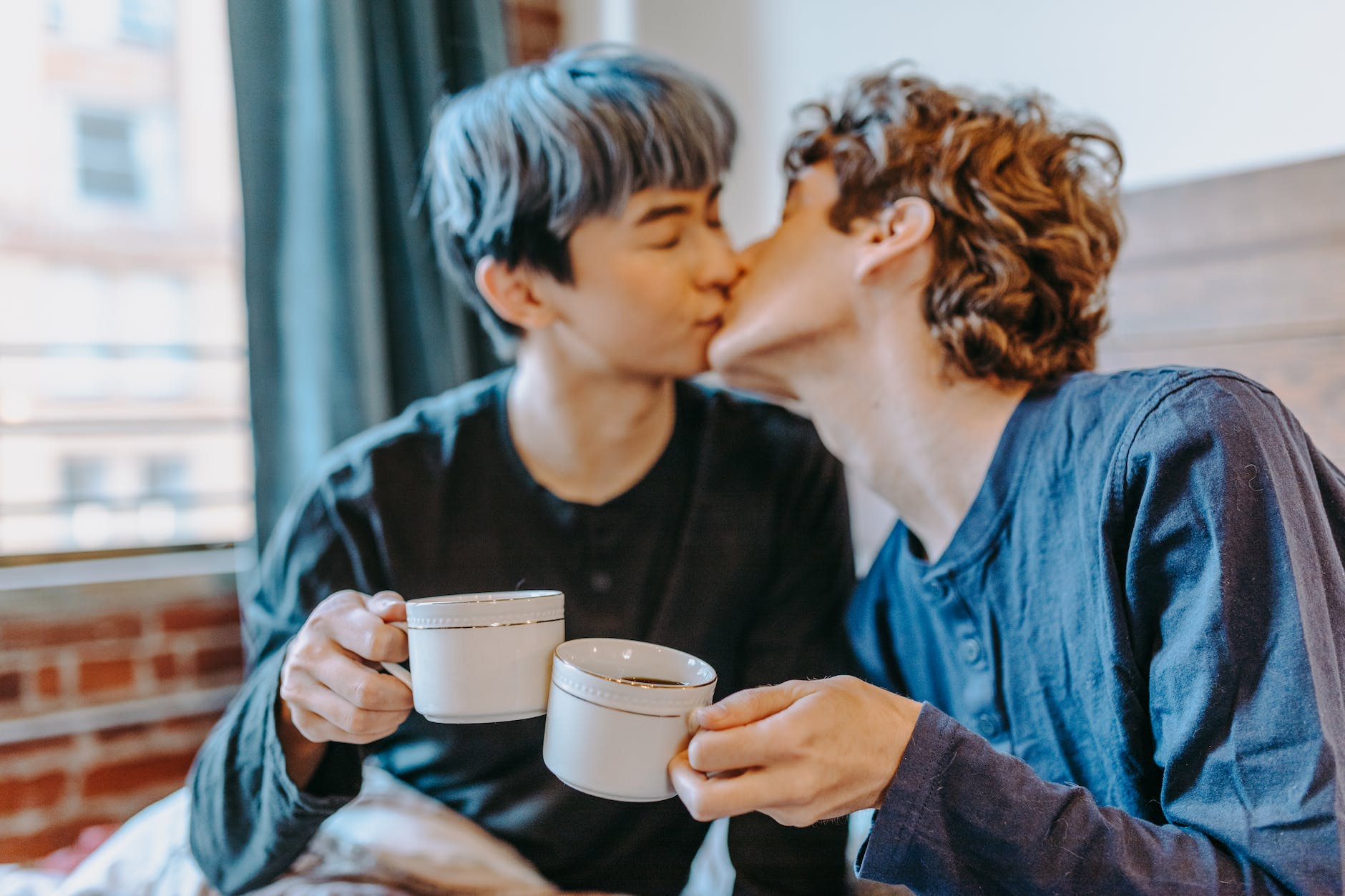 couple kissing while holding ceramic mugs