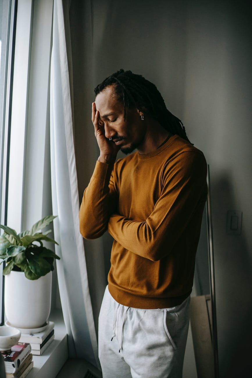 depressed black man touching face in frustration near window