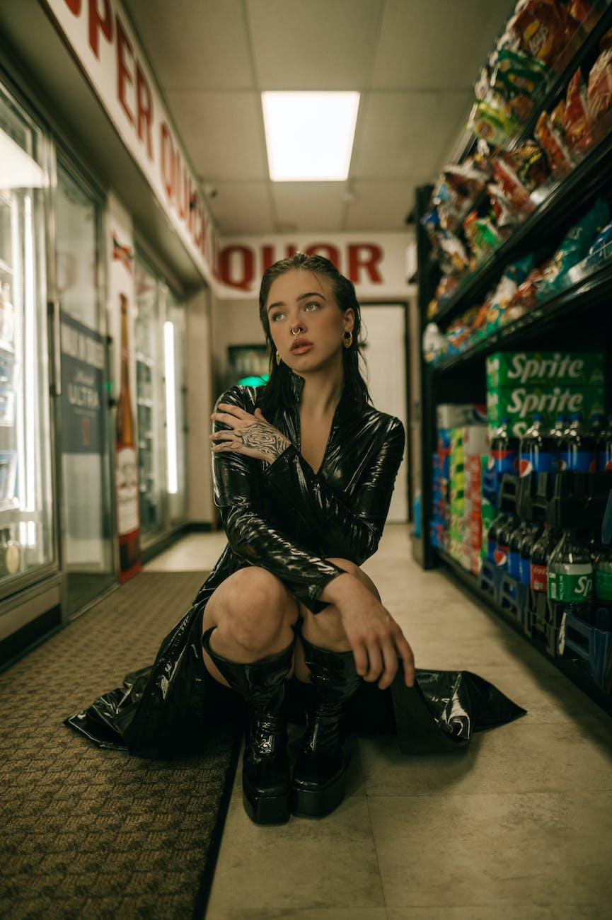 young woman in black pvc matrix style trench coat sitting on the floor at a supermarket aisle